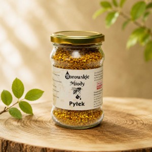 Słoik naturalnego pyłku pszczelego Borowskie Miody na drewnianym blacie, na tle z delikatnie rozmytymi zielonymi liśćmi.